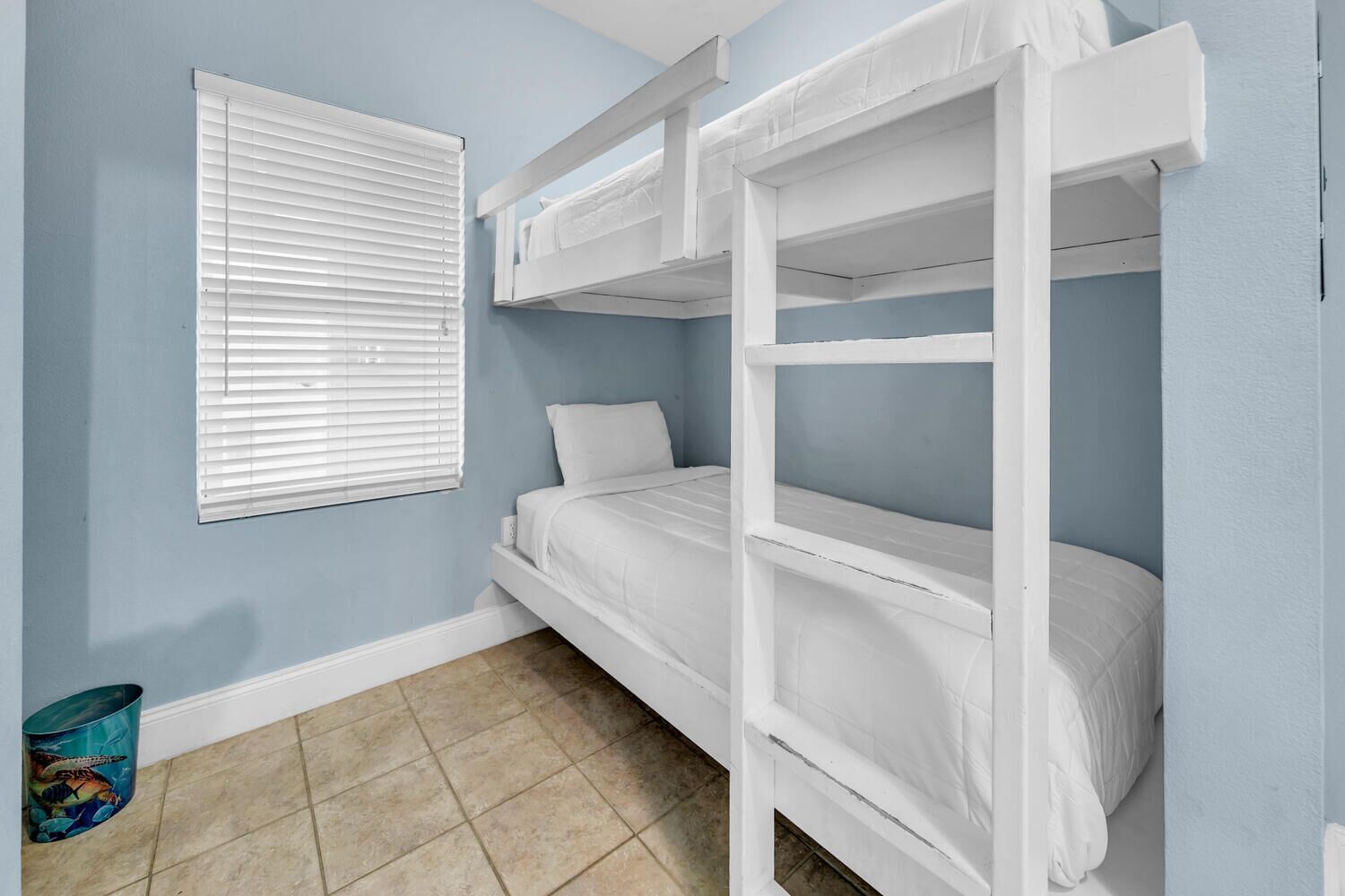 A bunk bed room with a window and a trash can.