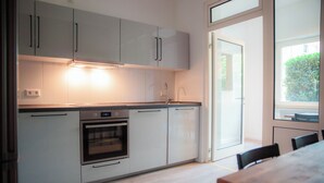 Une cuisine moderne avec des armoires blanches, un four encastré et un coin repas comprenant une table et des chaises en bois.