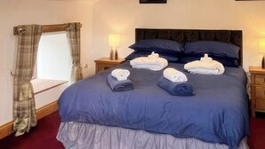 A neatly made bed with blue bedding, two bedside lamps, and a window with curtains.