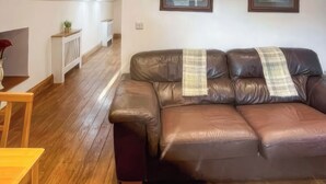 A brown leather sofa with a plaid throw blanket, a wooden coffee table, and a white radiator in a room with wooden flooring.