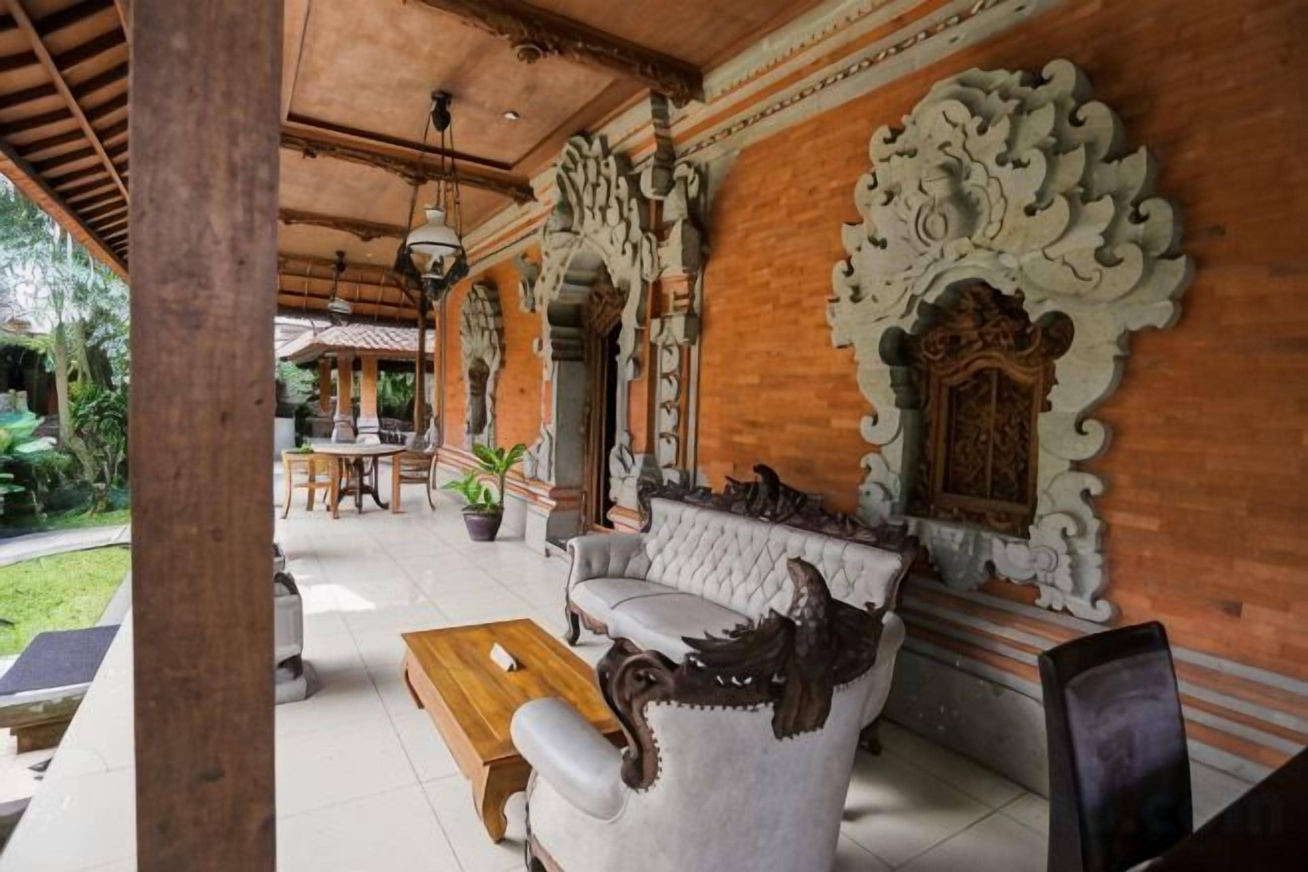 A covered outdoor seating area with a sofa and a wooden table, surrounded by ornate wall decorations and a potted plant.