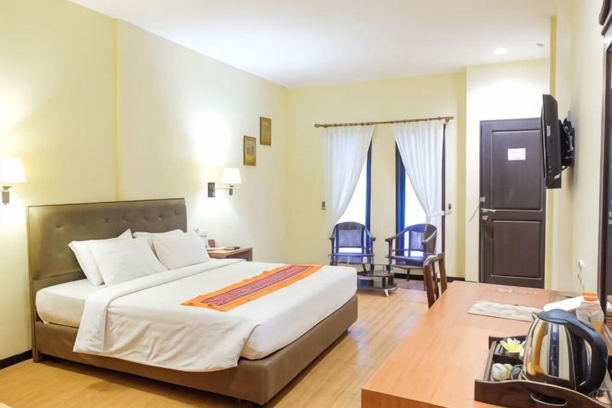 A hotel room with a bed, a desk, a chair, a TV, and a door.