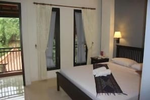 A bedroom with a bed, curtains, a nightstand, and a lamp. - Ubud Hotel & Cottages (Sukun)