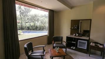 A hotel room with a large window, a desk, two chairs, a mirror, and a small table with a decorative item.