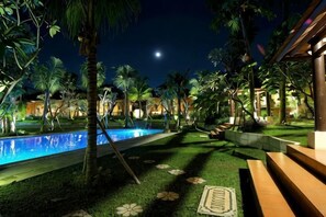 A nighttime resort pool area with a clear view of the pool, surrounding palm trees, and a moon in the sky. - Ubud Hotel & Cottages (Sukun)