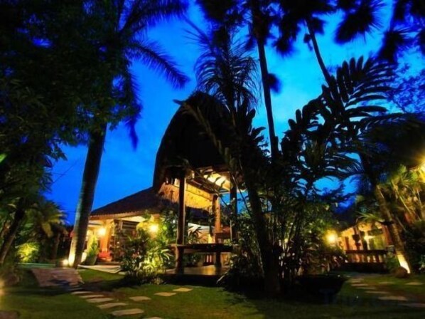 Un resort con un edificio de techo de paja, rodeado de palmeras y un sendero bien iluminado.