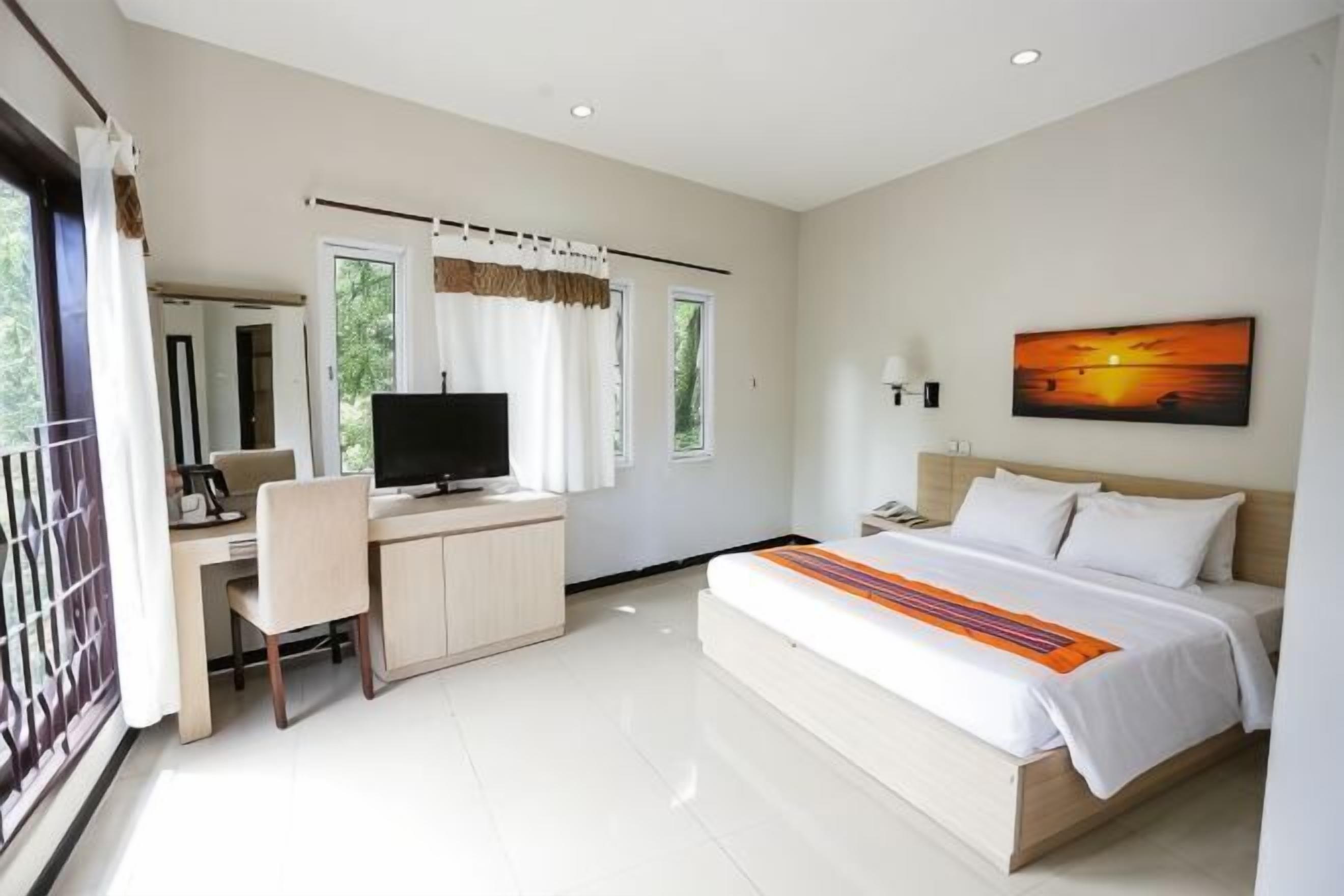 A modern hotel room with a bed, desk, chair, TV, and a painting on the wall.
