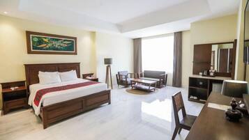 A hotel room with a large bed, a desk, a chair, a small table, and a television.