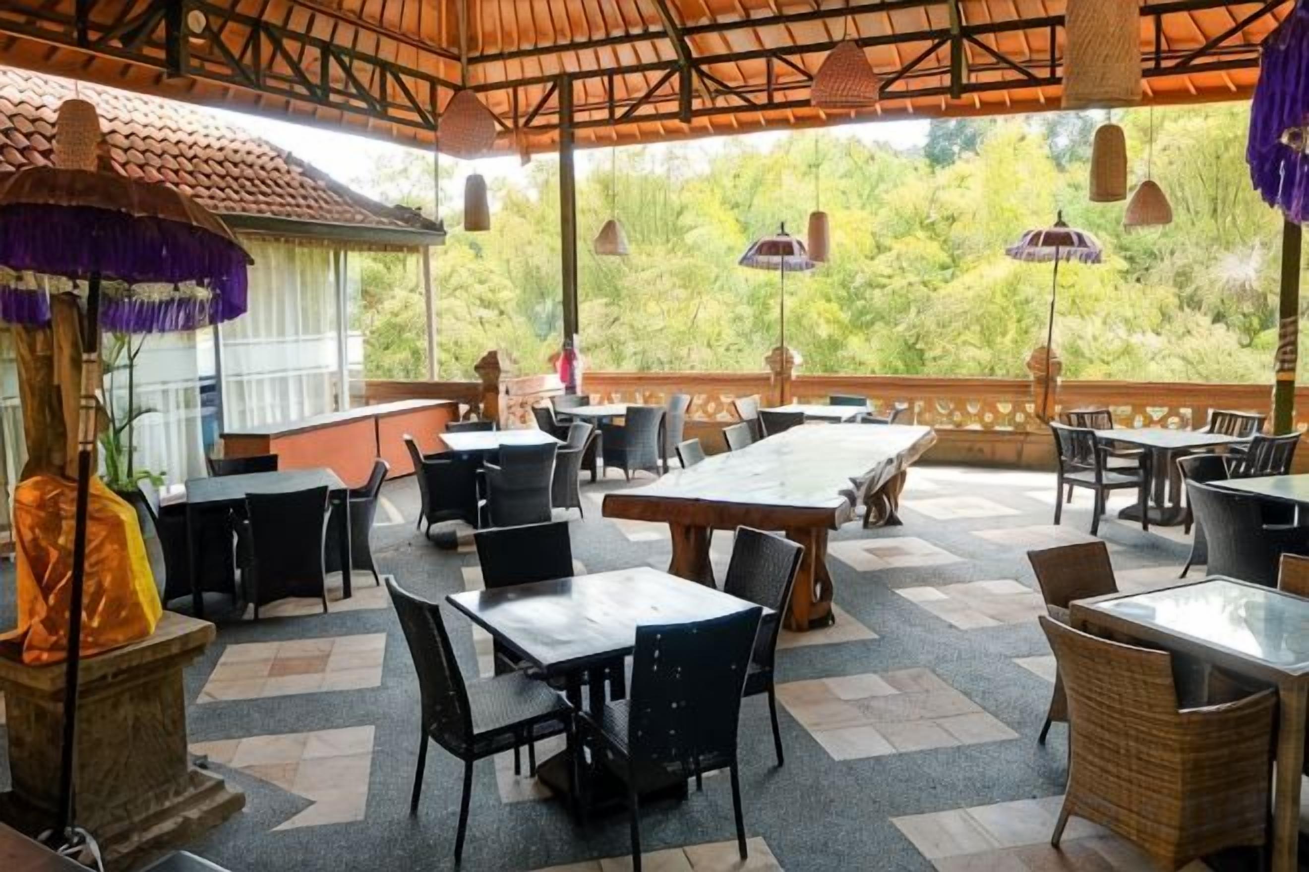 An outdoor dining area with tables and chairs, a stone pillar, and a view of greenery.