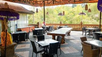An outdoor dining area with tables and chairs, a stone pillar, and a view of greenery.