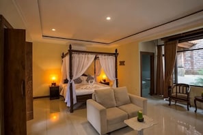 A bedroom with a four-poster bed, bedside tables, a sofa, and a view of the outside. - Ubud Hotel & Cottages (Sukun)