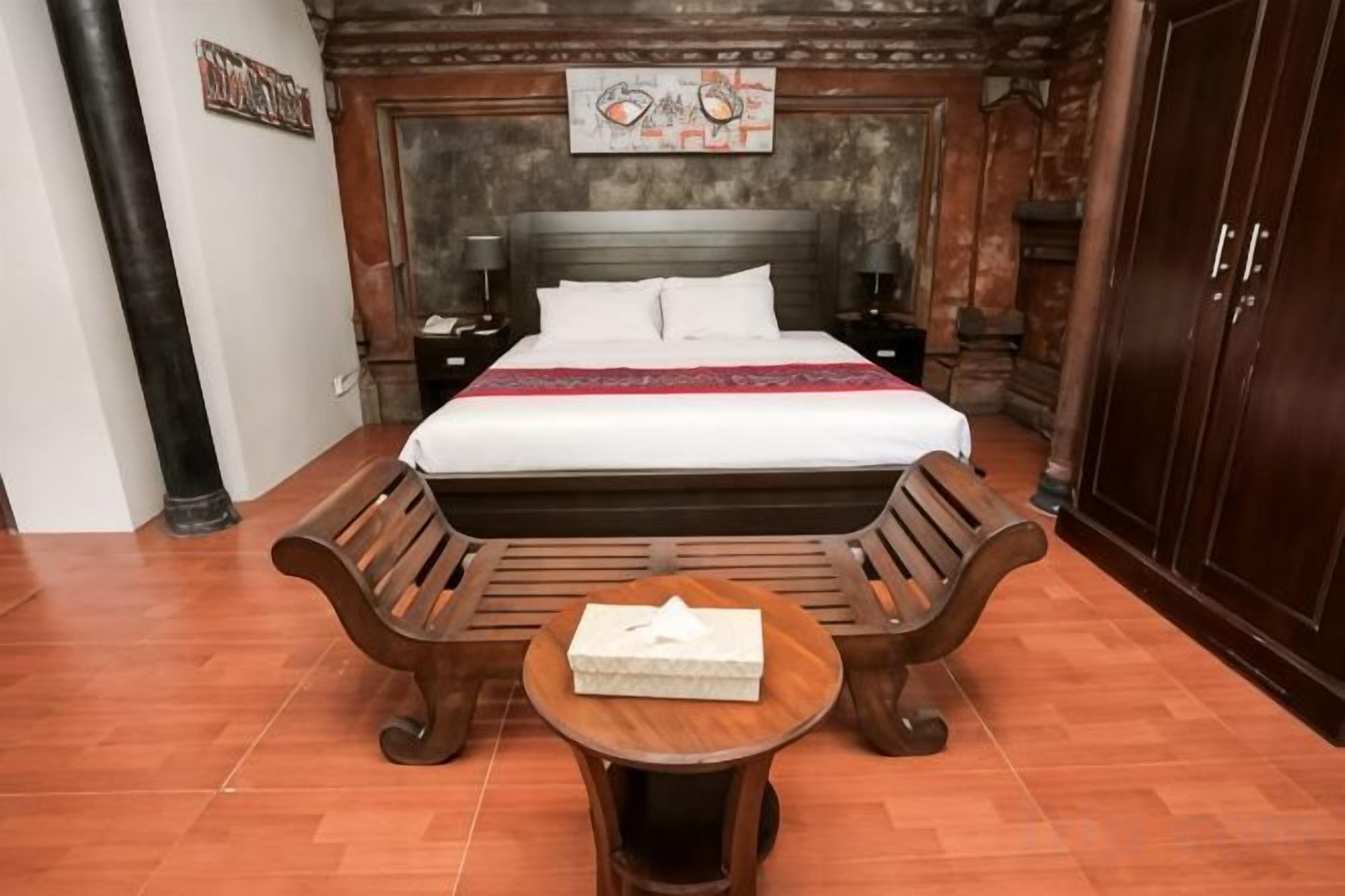 Une chambre avec un grand lit, des bancs en bois, une petite table et une table de chevet.