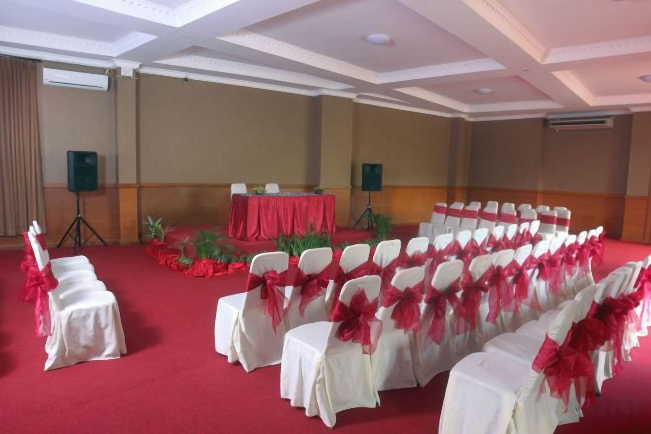 A conference room with rows of white chairs, red tablecloths, and a red carpet.