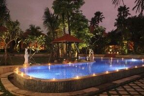 A swimming pool with a stone border, surrounded by palm trees and a gazebo. - Ubud Hotel & Cottages (Sukun)