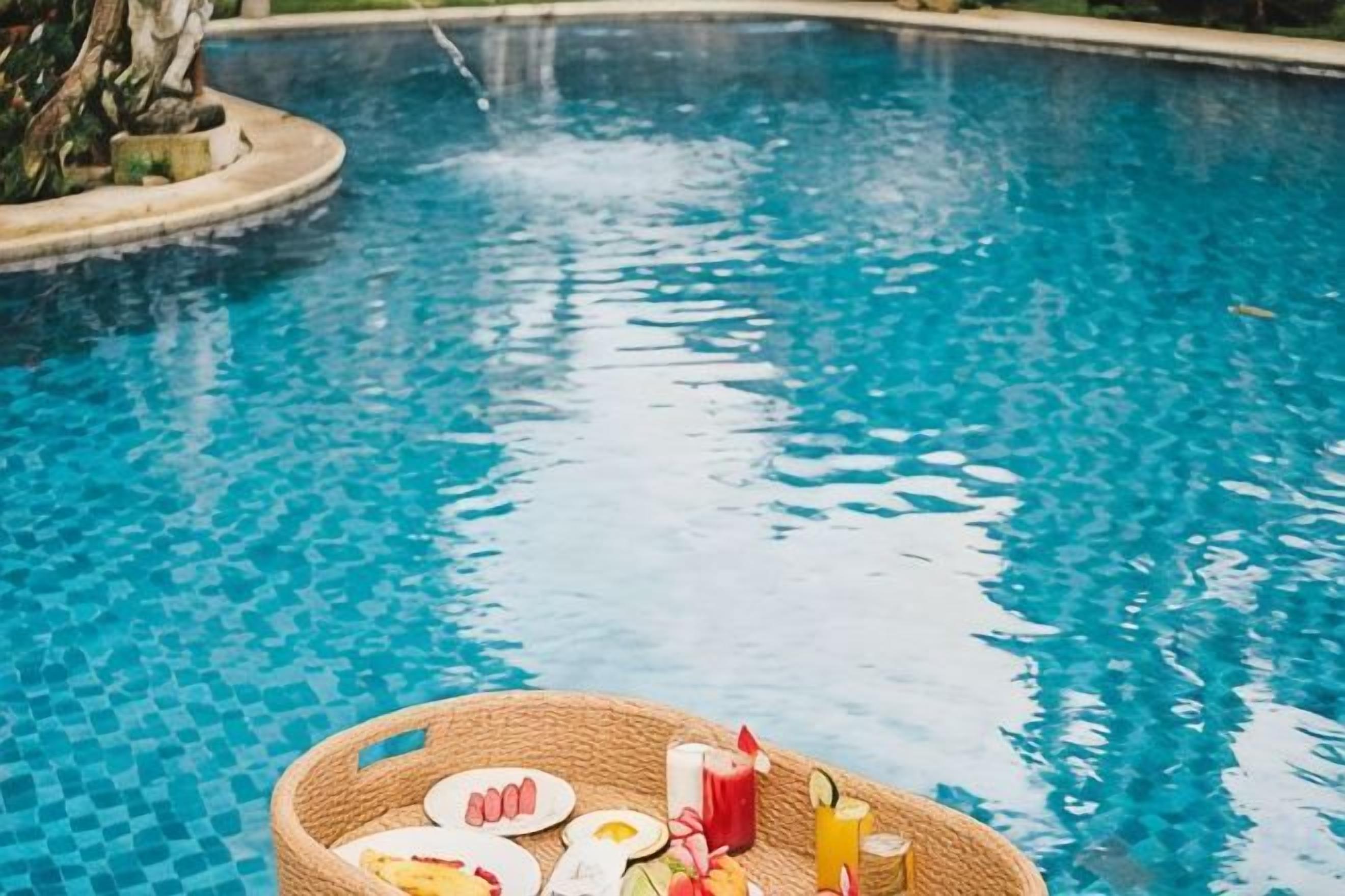 A pool with a floating tray containing food and drinks.