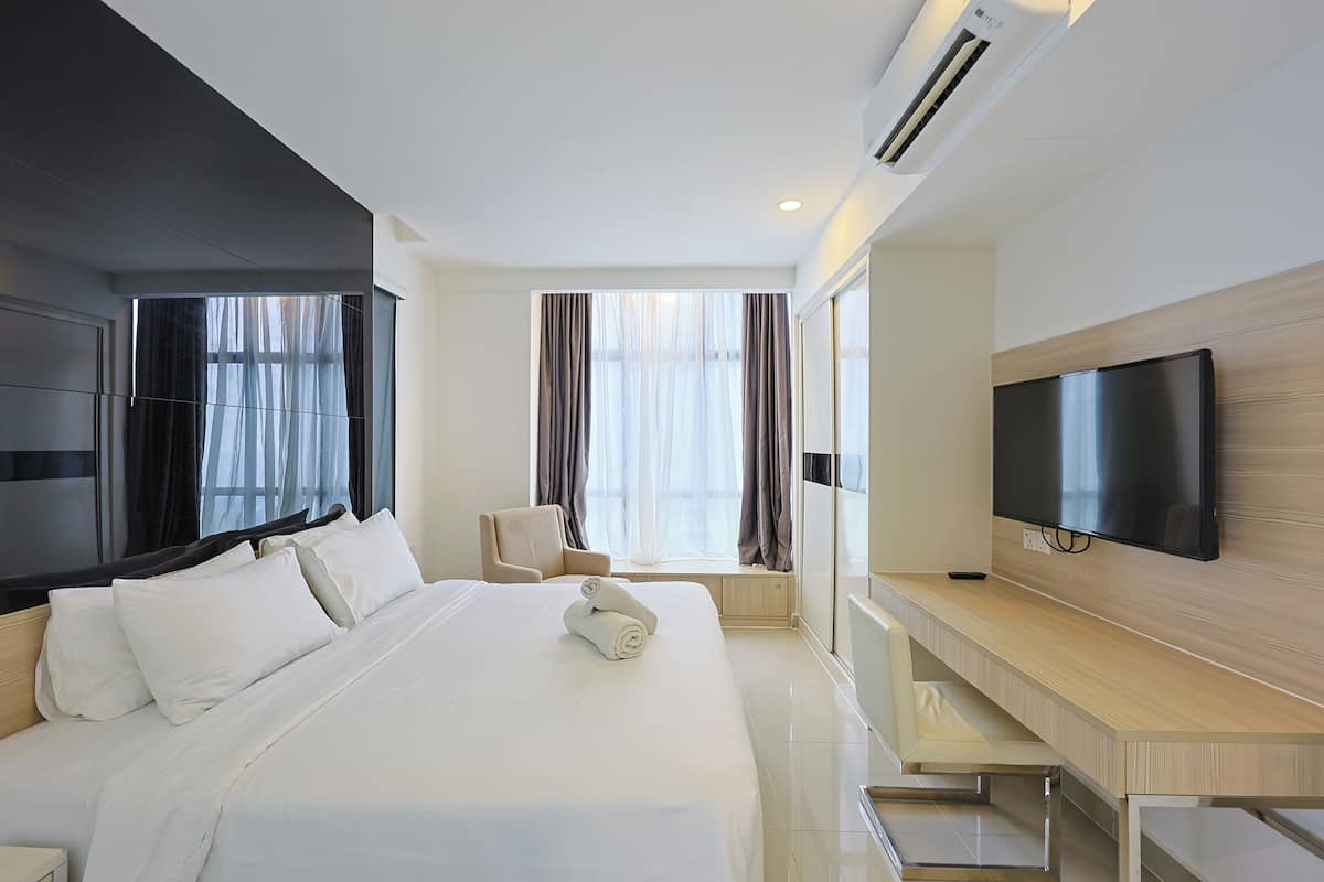A modern hotel room with a large bed, a TV, a desk, and a window with curtains.