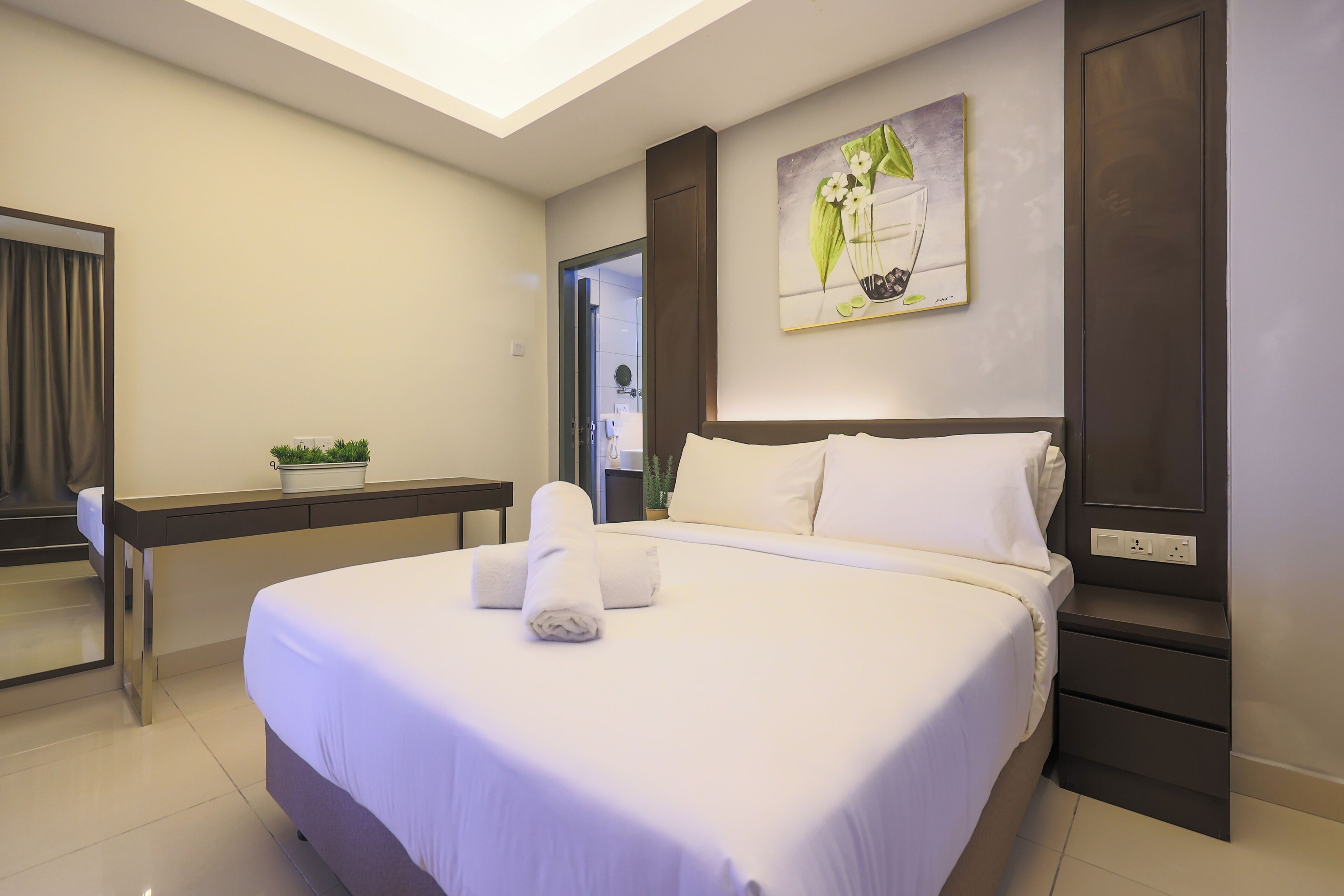 A modern hotel room with a large bed, a bedside table, a nightstand, and a painting on the wall.