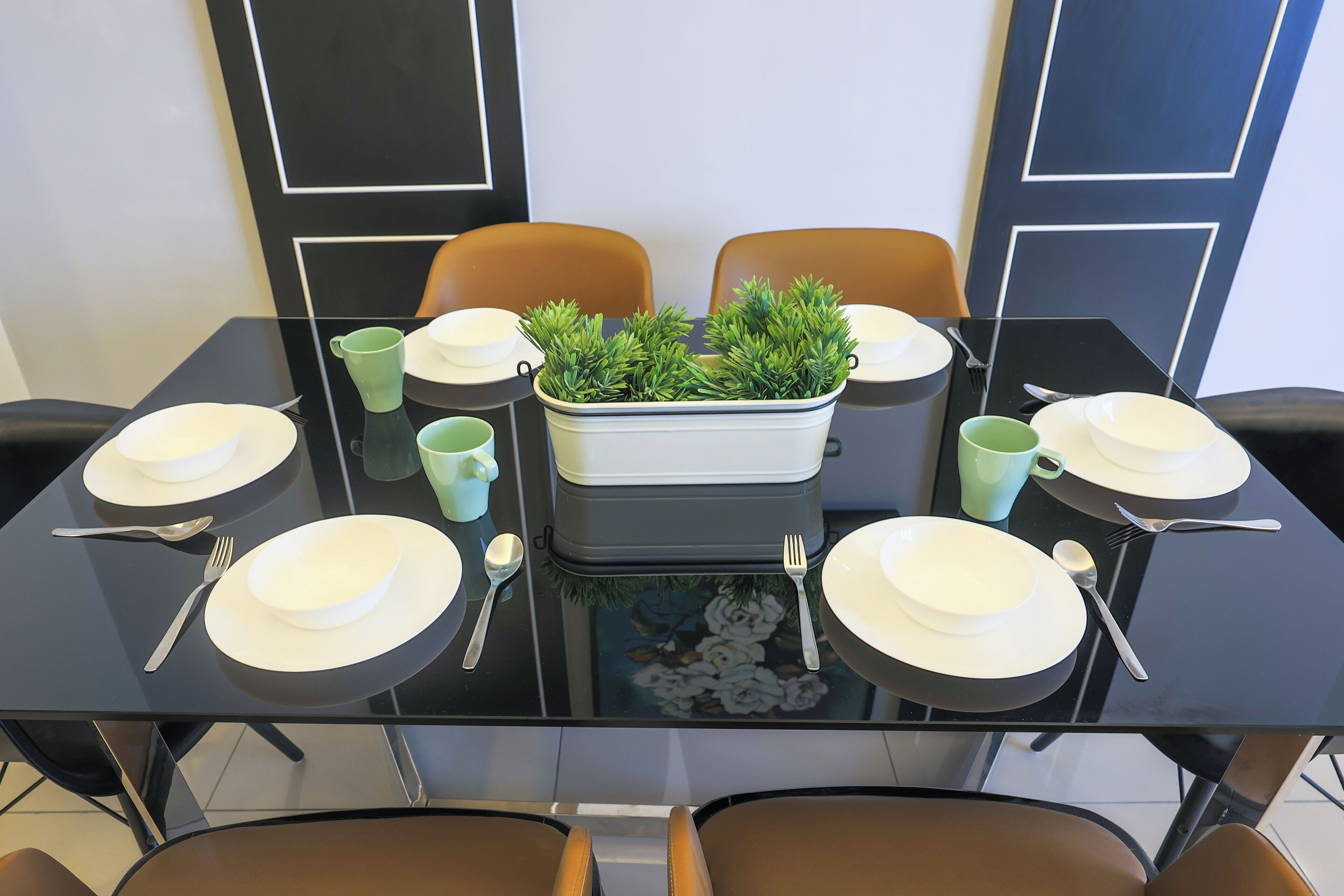 A dining table set with white plates, silverware, and a centerpiece of green plants in a white pot.