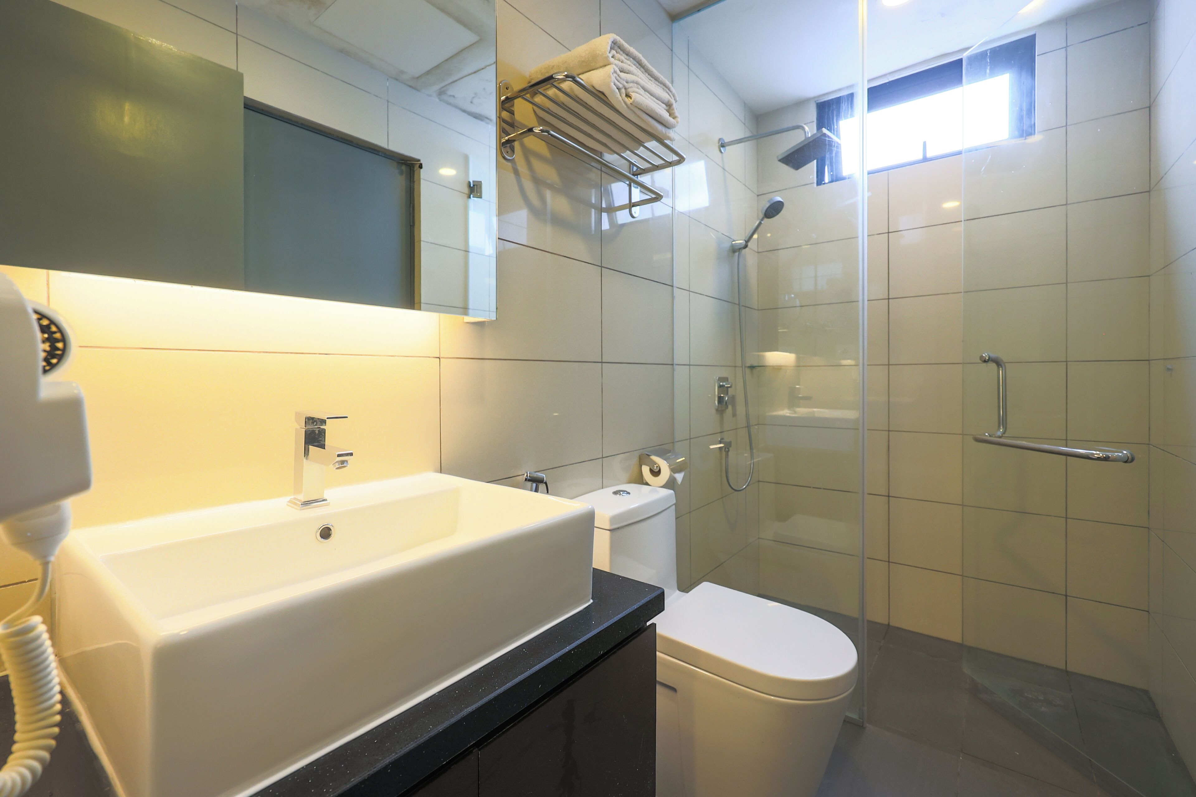 Une salle de bain moderne avec un grand lavabo blanc, des toilettes et une douche séparée par une paroi de verre.