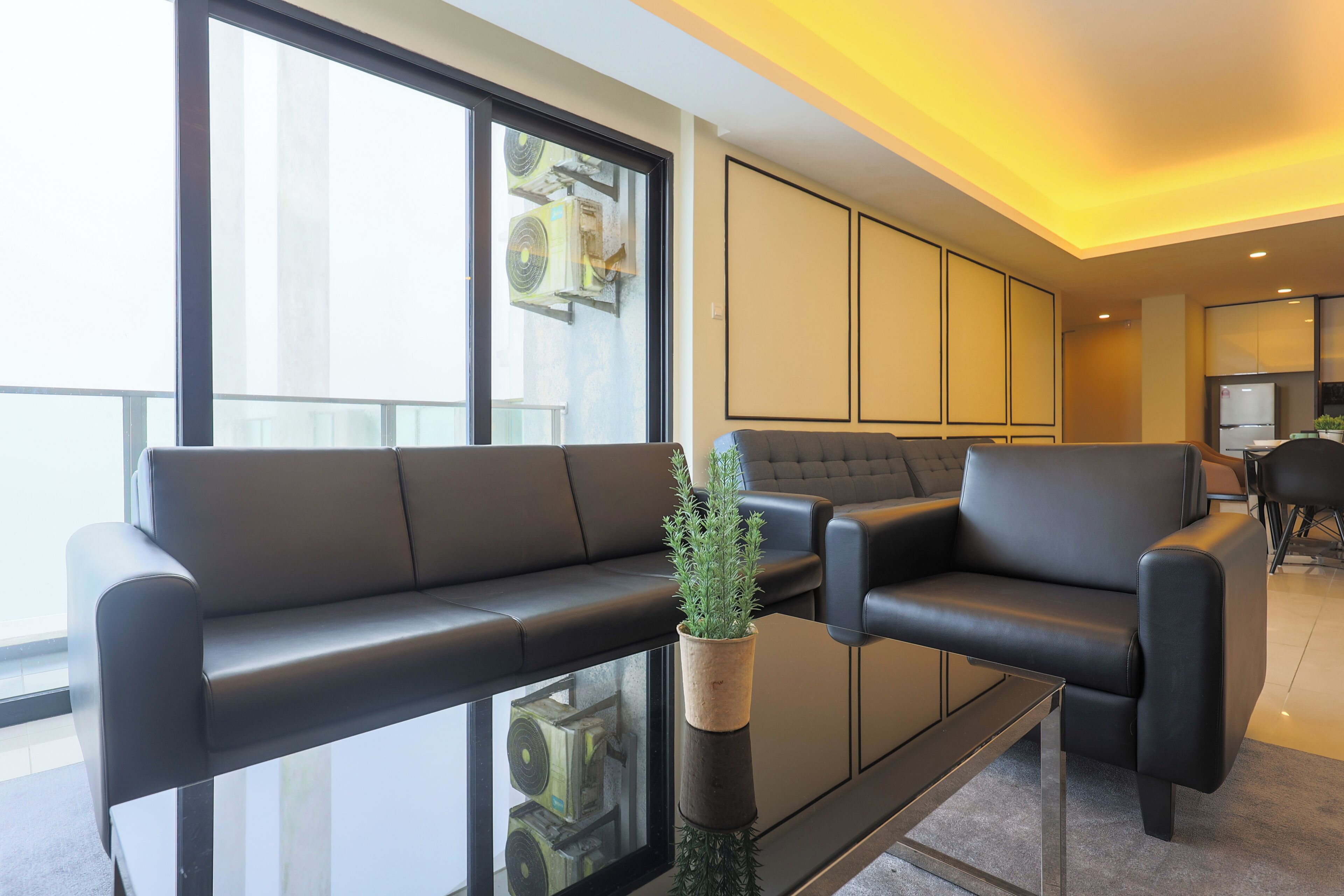 A modern living room with a black leather sofa, a glass coffee table, and a potted plant.