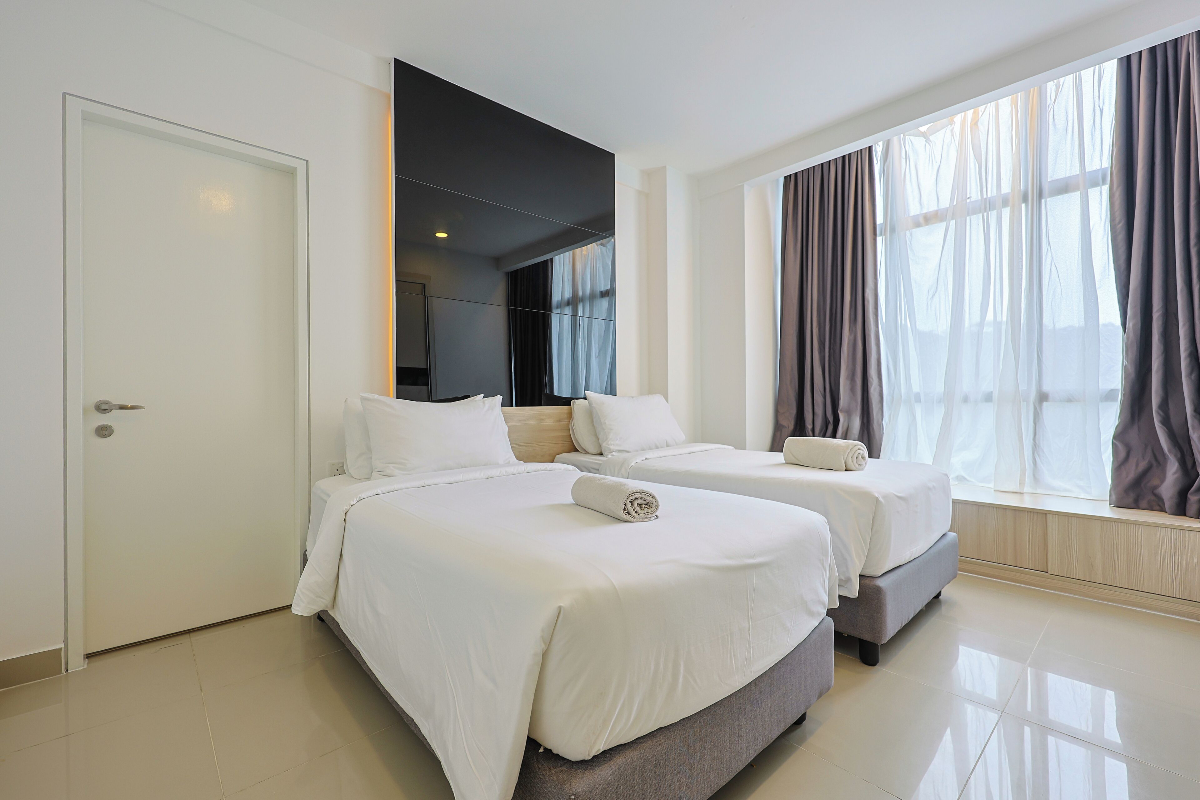 A hotel room with two beds, a large window with curtains, and a door.