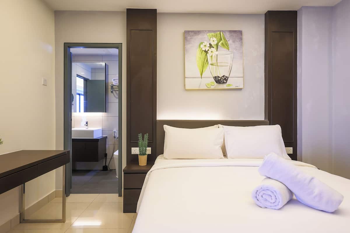 A hotel room with a bed, a nightstand, a small table, a potted plant, and a painting on the wall.