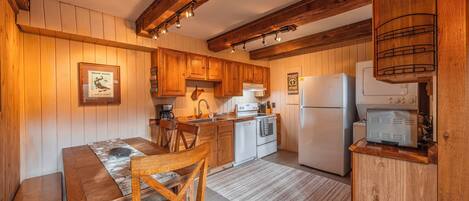 Una cocina rústica con armarios de madera, una mesa de comedor con sillas, un refrigerador y una cafetera.