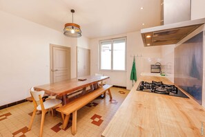 A kitchen with a wooden table, chairs, a gas stove, a hanging light fixture, and a window. - Suzanne's Grand House – Comfort & Tranquillity in Albi (Albi)