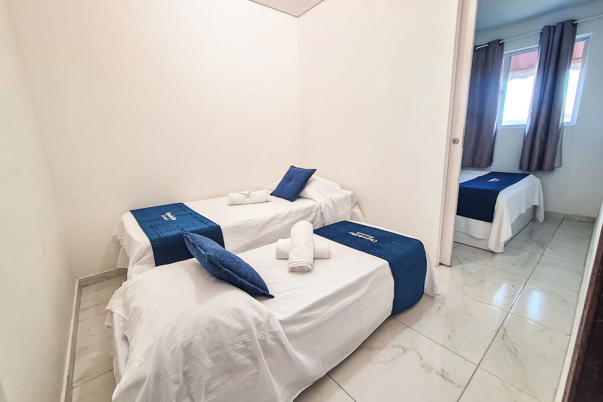 A hotel room with two beds, each with a blue bedspread and pillows, and a white towel on each bed.