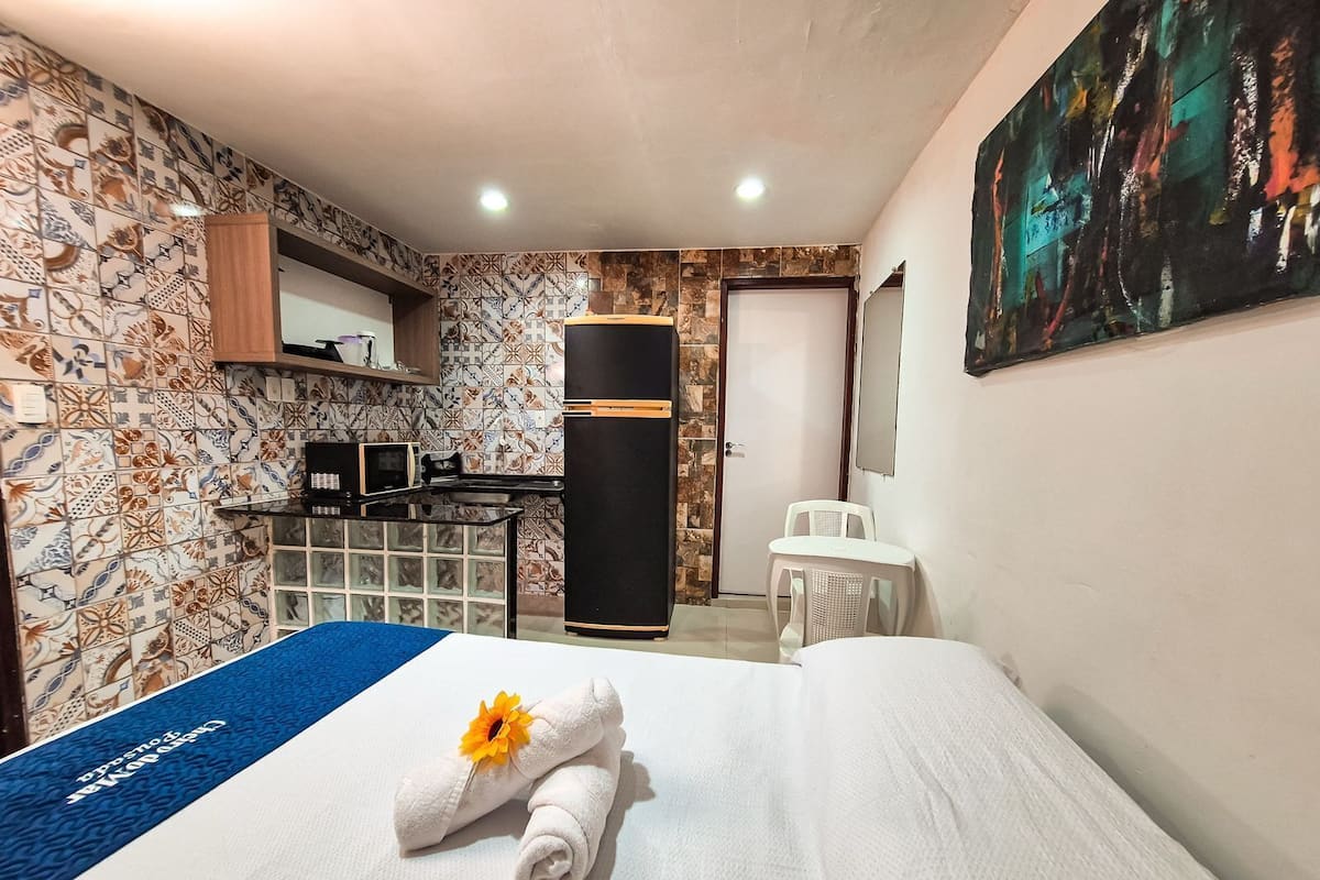 A hotel room with a bed, a desk with a computer, a refrigerator, and a painting on the wall.