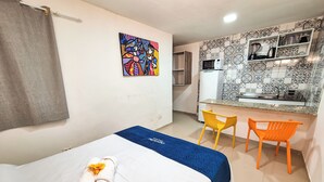 A hotel room with a bed, a desk, two chairs, a microwave, and a shelf with kitchen items. - Pousada Cheiro do Mar (Ipojuca)