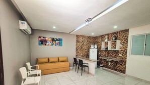 A modern kitchen with a microwave, sink, and a refrigerator. There is a brown sofa and two white chairs in the living area. - Pousada Cheiro do Mar (Ipojuca)