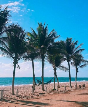 A beach with palm trees and a hammock. - Pousada Cheiro do Mar (Ipojuca)