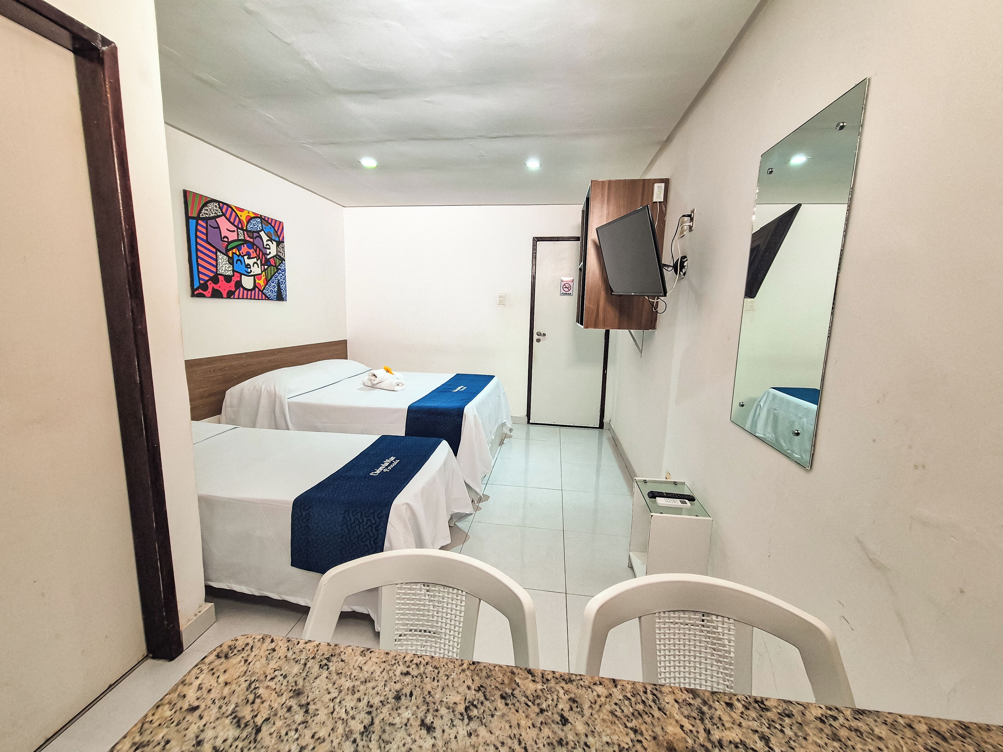 A hotel room with two beds, a television, a mirror, and a small table with chairs.