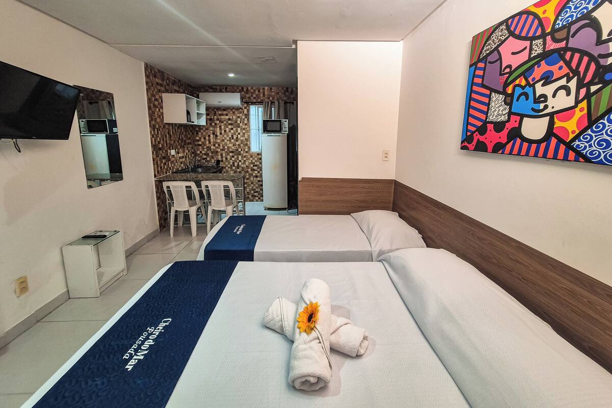 A hotel room with two beds, a TV, a kitchenette, and a painting on the wall.