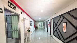 A hallway with a sign reading "SAÍDA" on the left, a small table with flowers, and a fire extinguisher on the right. - Pousada Cheiro do Mar (Ipojuca)