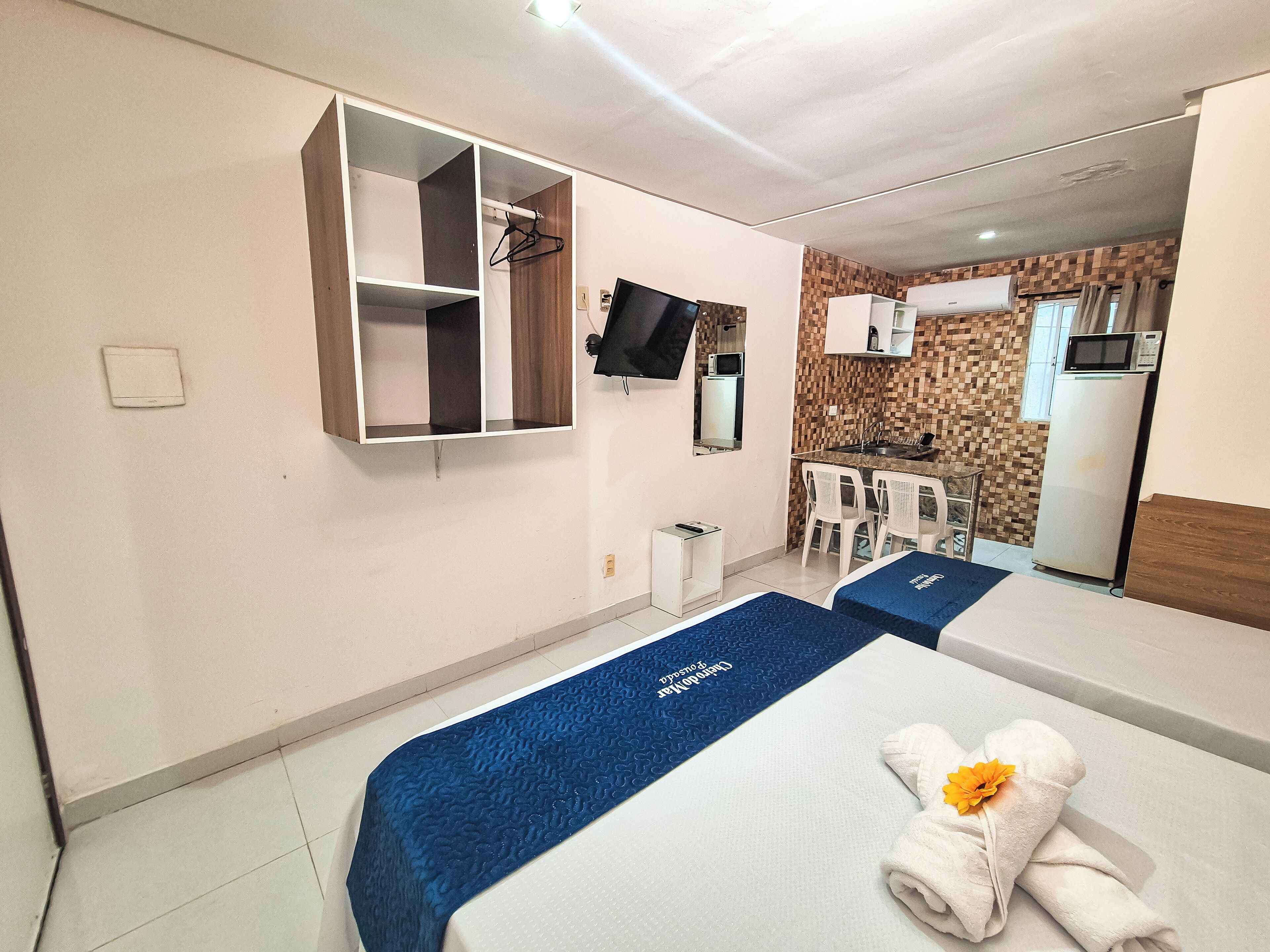 Une chambre d’hôtel avec deux lits, une télévision, une armoire, un petit coin cuisine et une salle de bain.