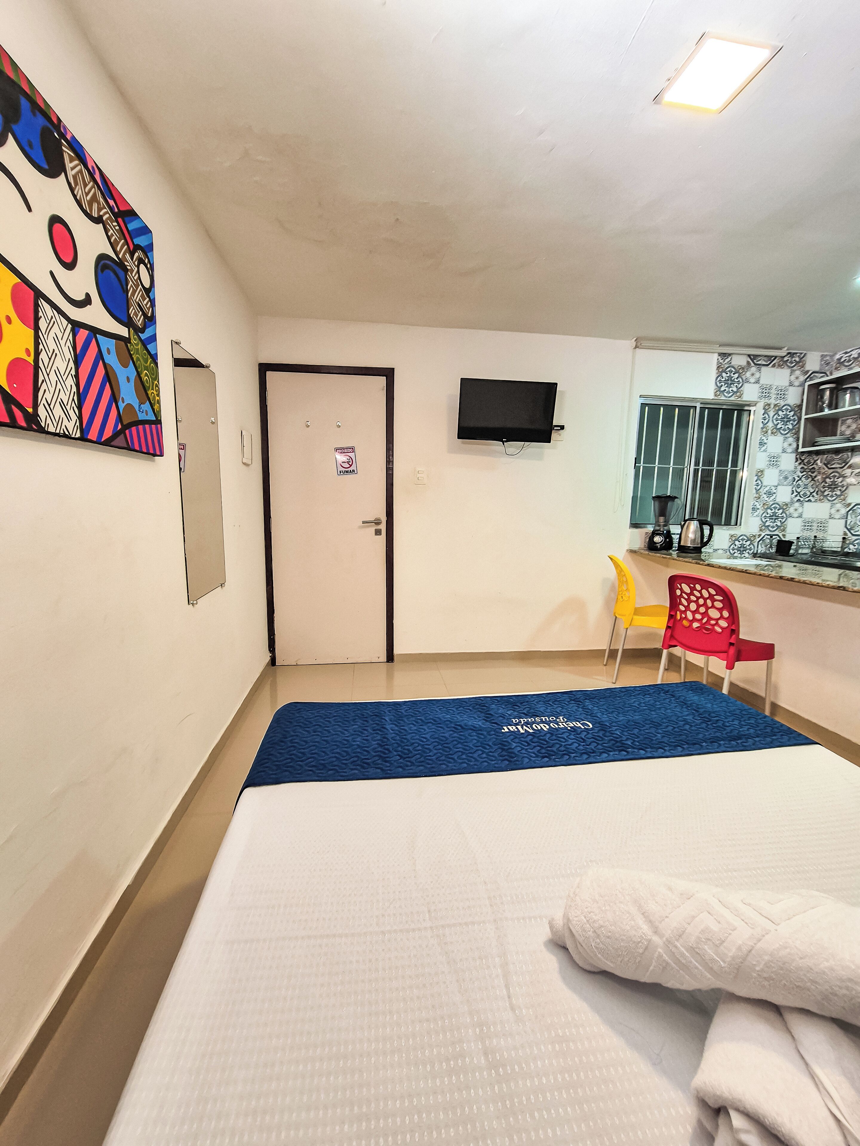 Habitació d'hotel amb un llit, un estora blava, una televisió, una porta i una finestra amb vista a l'exterior.