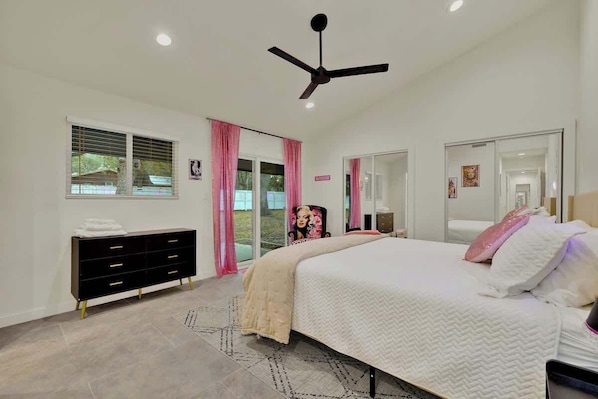A bedroom with a bed, a dresser, a ceiling fan, and a window with curtains.