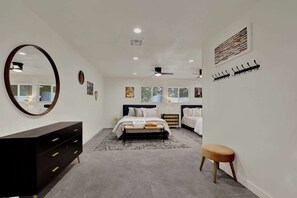 Une chambre à coucher moderne avec un grand miroir, un lit avec une tête de lit, une table de chevet, un petit tabouret et un porte-manteau fixé au mur.