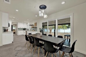A modern kitchen with white cabinets, a dining area with a long table and black chairs, and a large sliding glass door leading to an outdoor area.