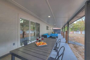 Eine Terrasse im Freien mit einem Holztisch, gedecktem Esstisch, einem blauen Sofa und einer Glastür, die in einen Garten führt.