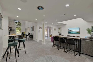 A modern kitchen with bar stools, a dining area with a round table, and a living room with a sofa and TV. - Walk to Whitewater Amphitheater-GameRoom & Firepit (Canyon Lake)