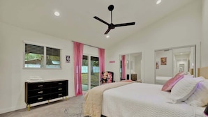 Une chambre à coucher avec un lit, une commode, un ventilateur de plafond et une fenêtre avec des rideaux.