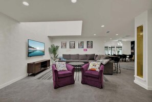 A modern living room with a grey sofa, two purple armchairs, a coffee table, and a TV on the wall. - Walk to Whitewater Amphitheater-GameRoom & Firepit (Canyon Lake)