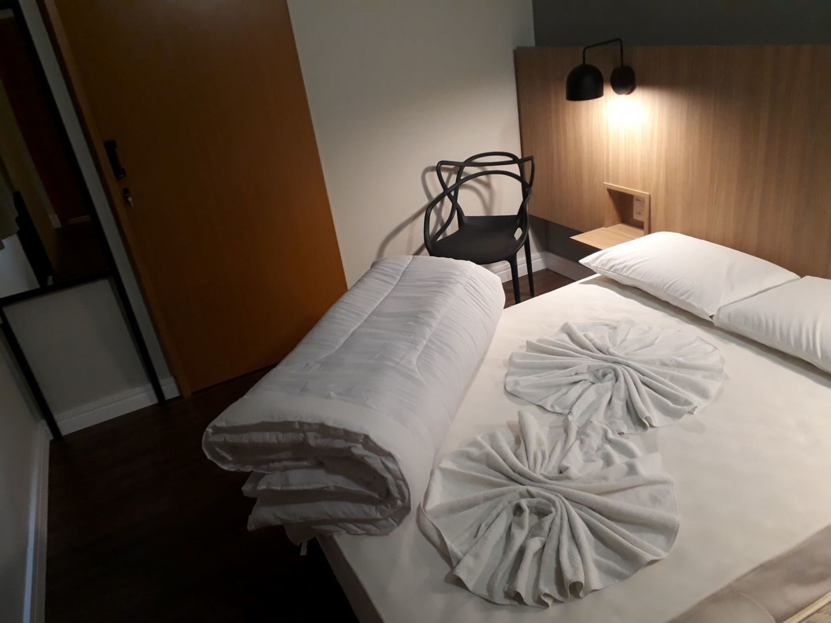 Een hotelkamer met een bed, een stoel en een houten hoofdeinde.
