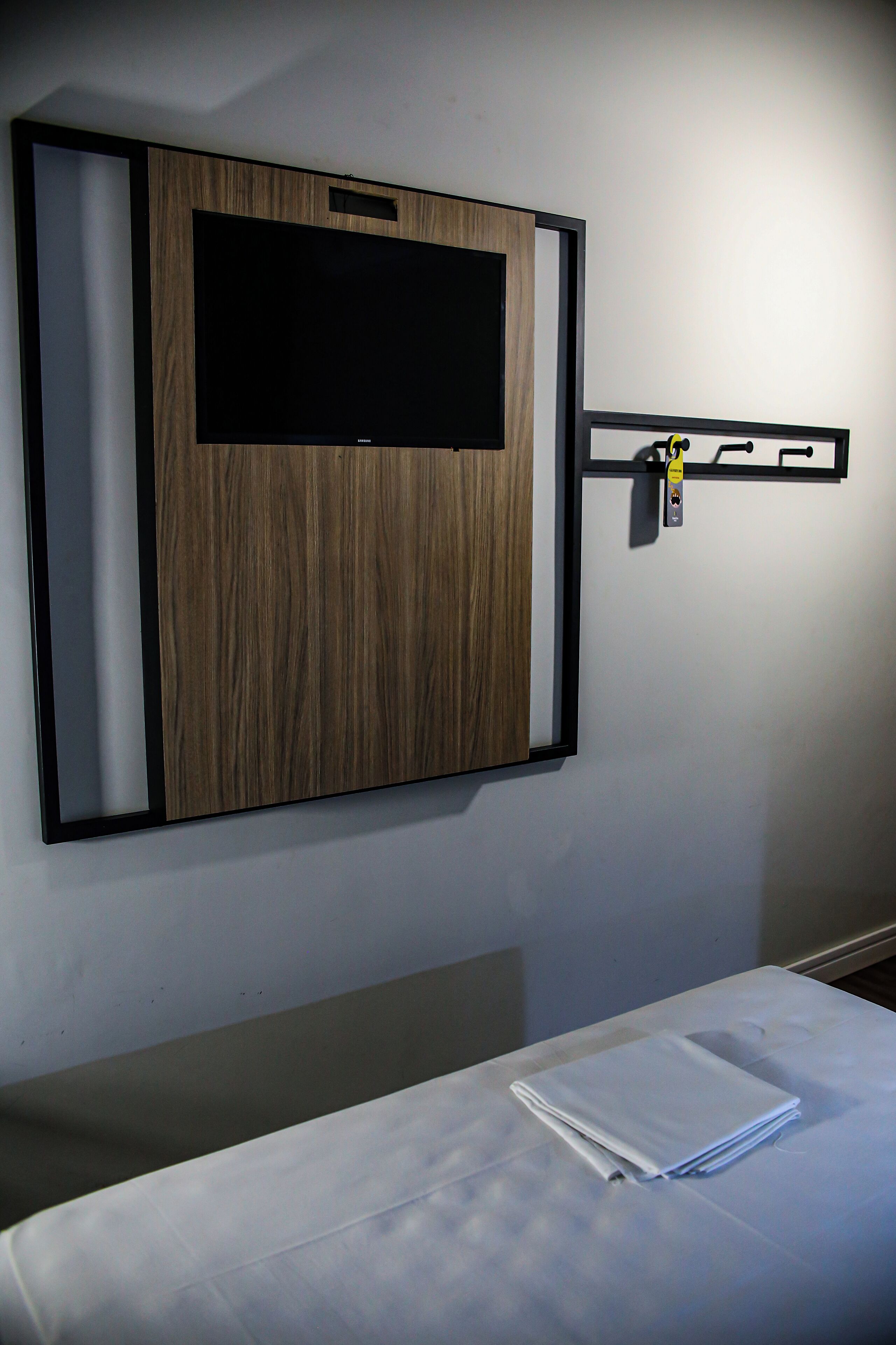 Una habitación con televisión instalada, pared de paneles de madera y cama con una manta blanca doblada.