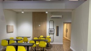 A modern conference room with yellow chairs and tables, wooden paneling on the back wall, and an air conditioning unit. - Hotel Graal Inn Uberaba (Uberaba)