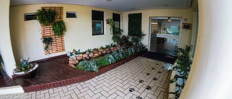 A hotel lobby with a herringbone-patterned floor, a reception desk, a plant wall, and a small water feature.