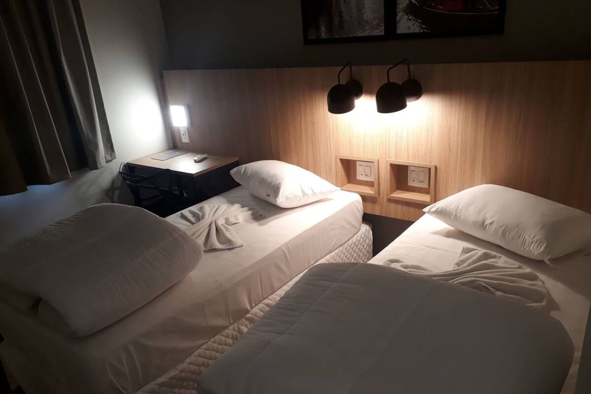 Une chambre d’hôtel avec deux lits, un bureau et un luminaire fixé au mur.